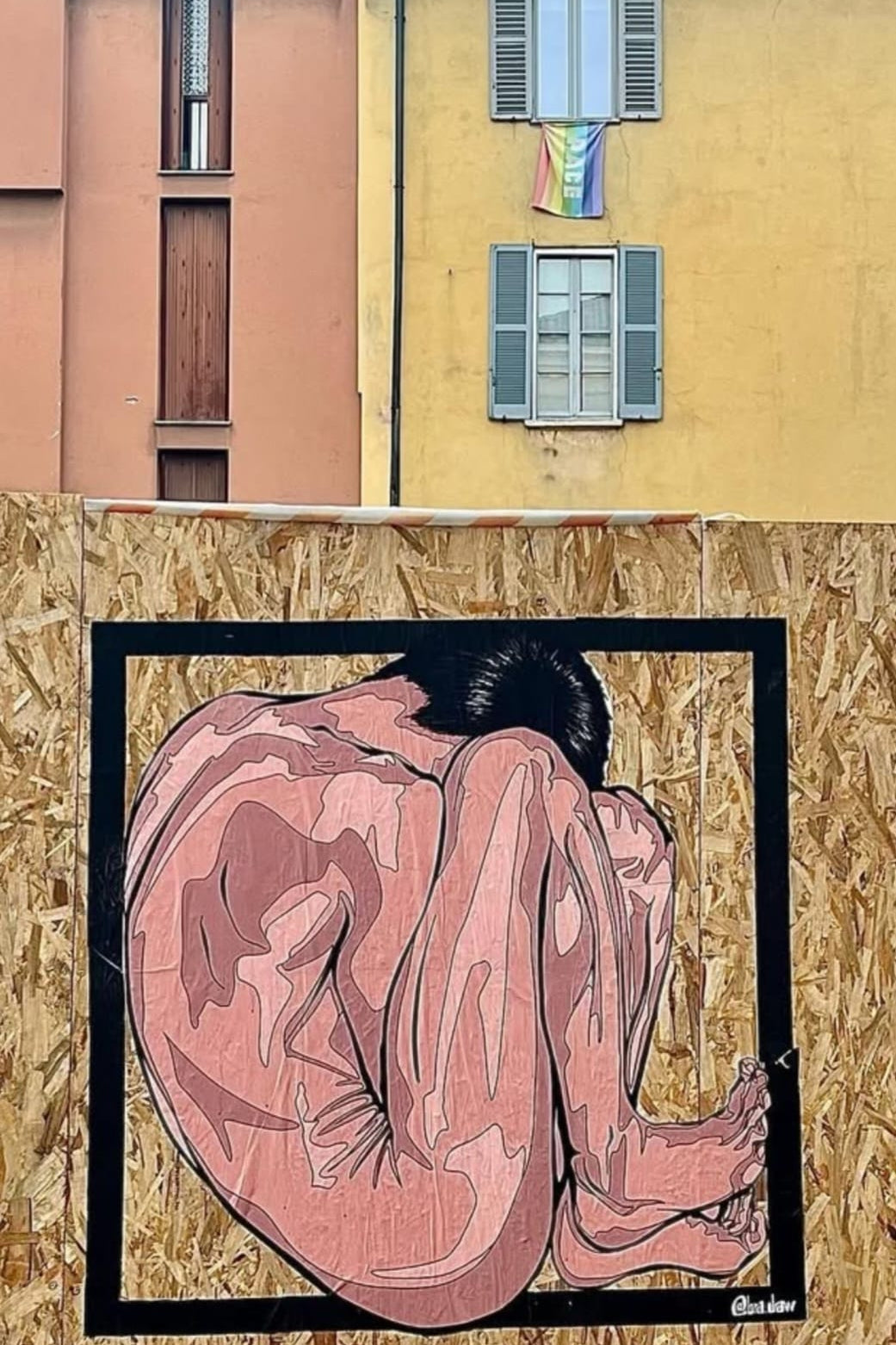 Artistic depiction of a person sitting with a rainbow flag on a building in the background.